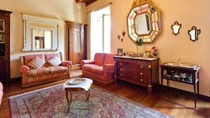 A cozy living room with a plaid sofa, a matching armchair, a wooden coffee table, and a large ornate mirror on the wall.