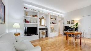 A living room with a white sofa, a fireplace, a TV, and a dining area with a table and chairs. - Downtown Rome, Vatican - St. Peter's area.  Elegant 3-bedroom, 2-bathroom apartment (Roma)