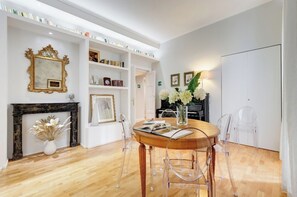 A dining area with a round table, clear chairs, a fireplace, and a bookshelf.