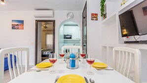 Un comedor con una mesa blanca dispuesta para cuatro personas, con platos amarillos y copas de vino tinto.
