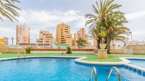 Una piscina con borde curvo, rodeada por una cerca blanca y palmeras.