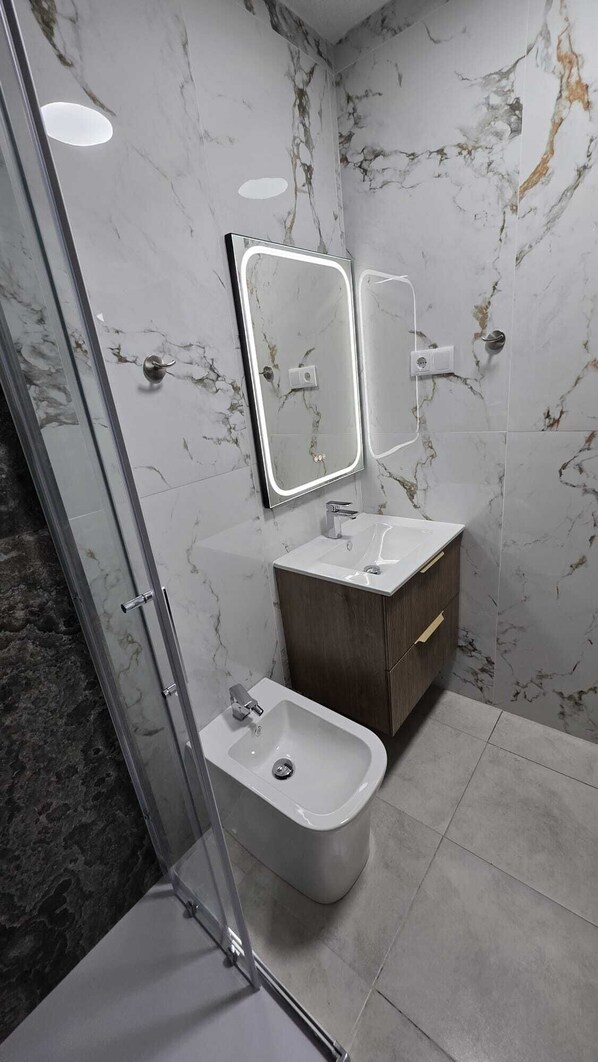 A bathroom with a marble wall, a glass shower enclosure, a bidet, and a vanity with a mirror. - Ideal for Families, Couples or Friends - apartment with pool, near beach (Alicane)