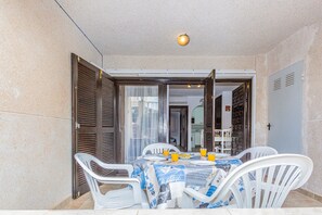 A small patio with a table set for two, white plastic chairs, and a tablecloth with a nautical theme.