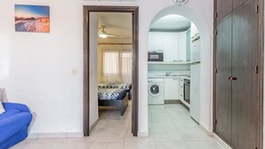 Un espacio habitable compacto con kitchenette, lavadora y cama con ropa de cama estampada.