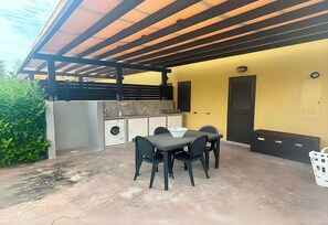 Un espace cuisine extérieur avec une table et des chaises, un lave-linge et une porte.