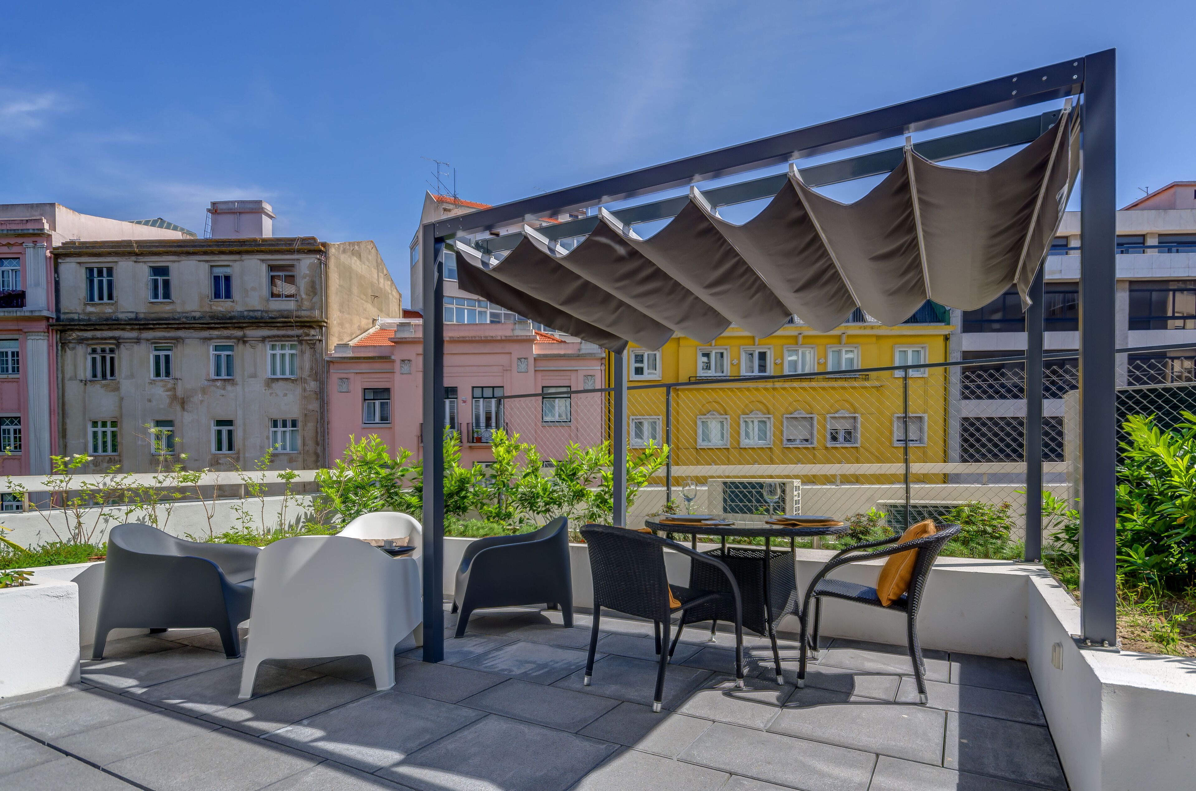 Eine Terrass mit moderner Möbel, einer Pergola und Blick auf farbenfrohe Häuser.