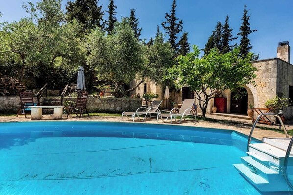 Una piscina con sillones de descanso y un edificio de piedra al fondo.