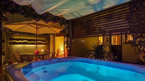 A hot tub with a blue light, surrounded by wooden furniture and plants. - Apartment with Garden and Jacuzzi. Sea view. Fully equipped. (Lagoa - Açores)