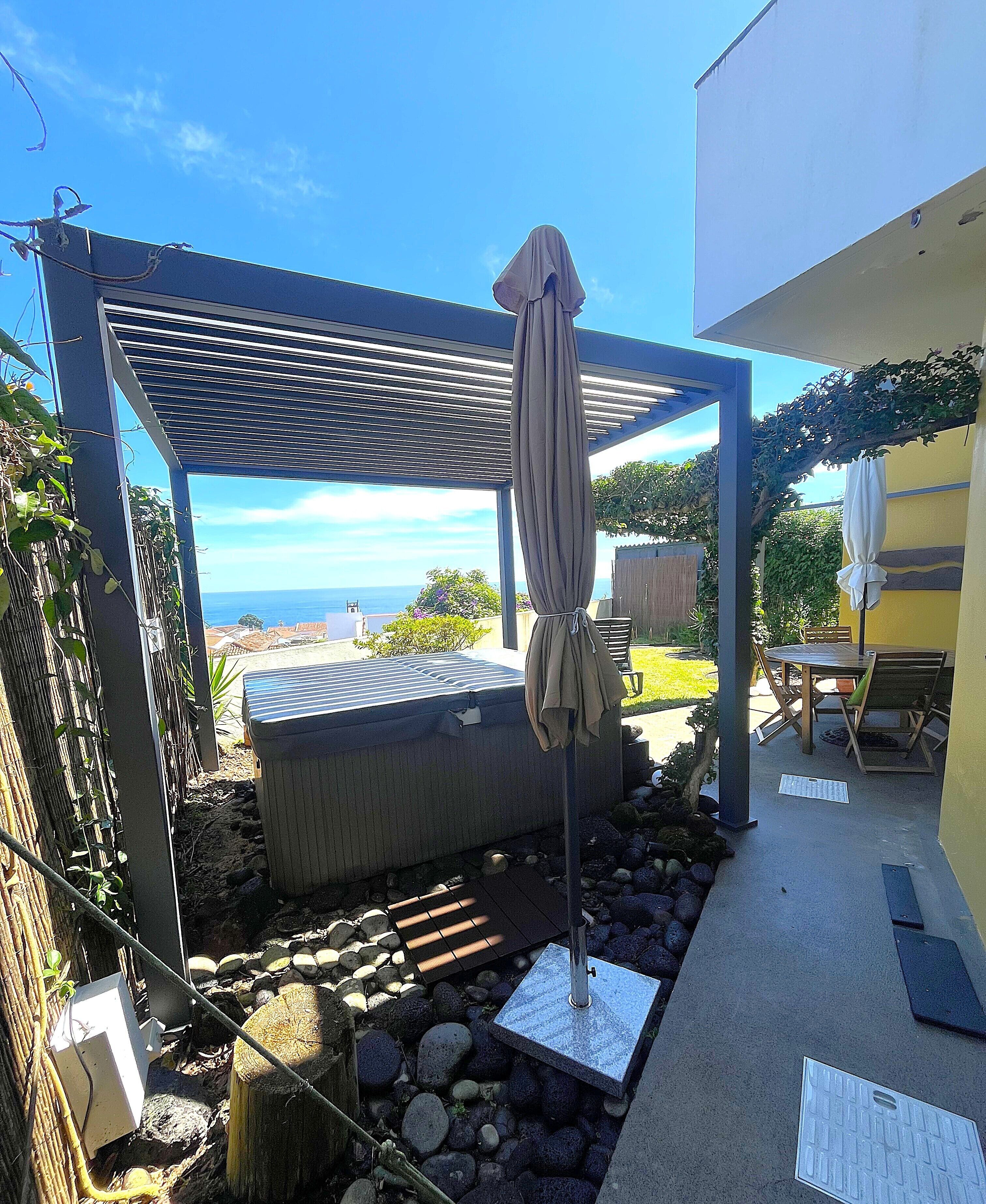 A covered outdoor seating area with a hot tub, a pergola, and a view of the ocean.
