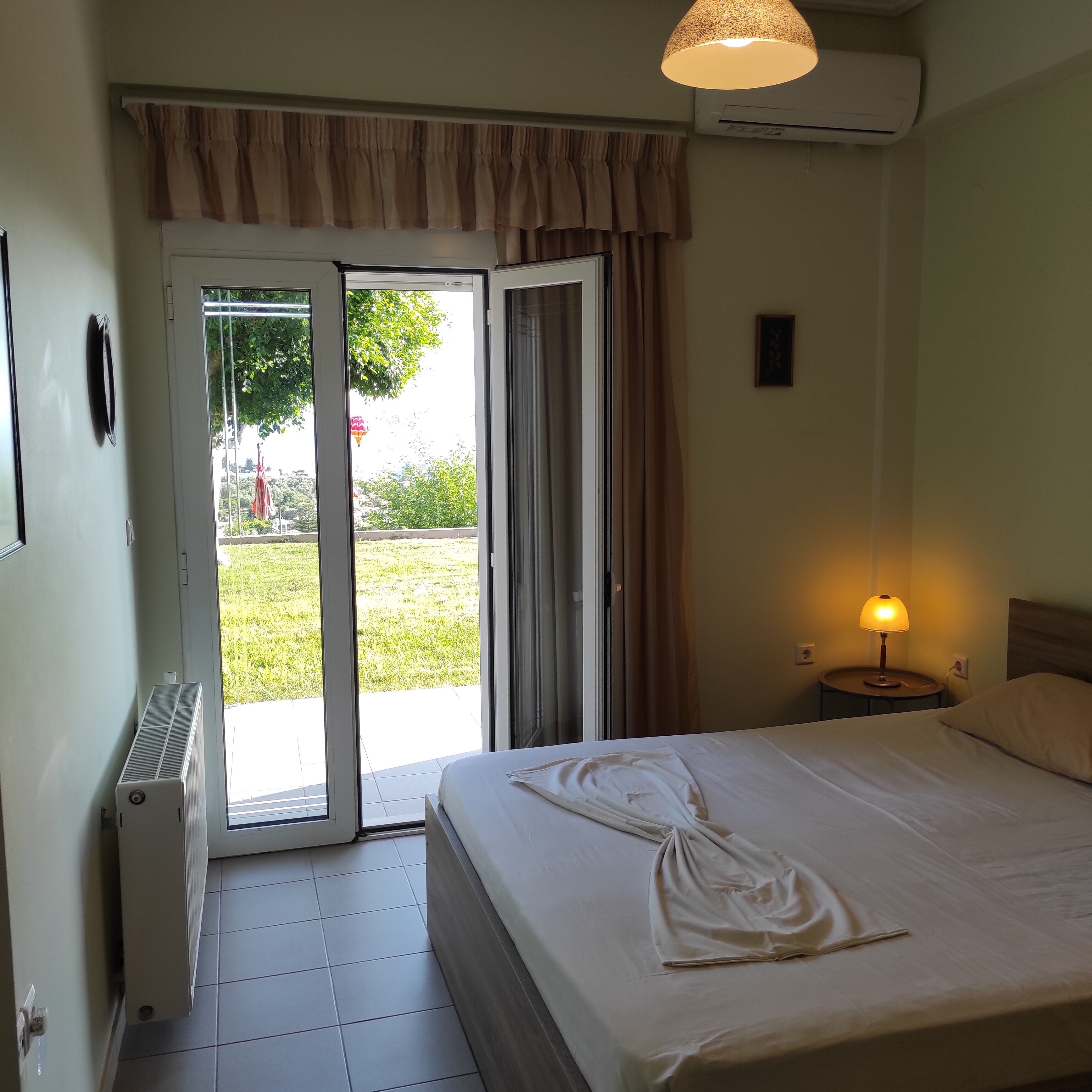 Une chambre d’hôtel comprenant un lit, une table de chevet avec une lampe, une fenêtre avec des rideaux et un appareil de climatisation.