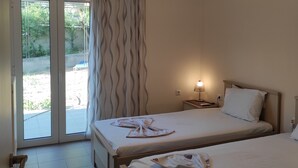 Une chambre d’hôtel avec deux lits, une porte-fenêtre coulissante donnant sur un espace extérieur, une table de chevet avec une lampe et un appareil de climatisation fixé au mur.