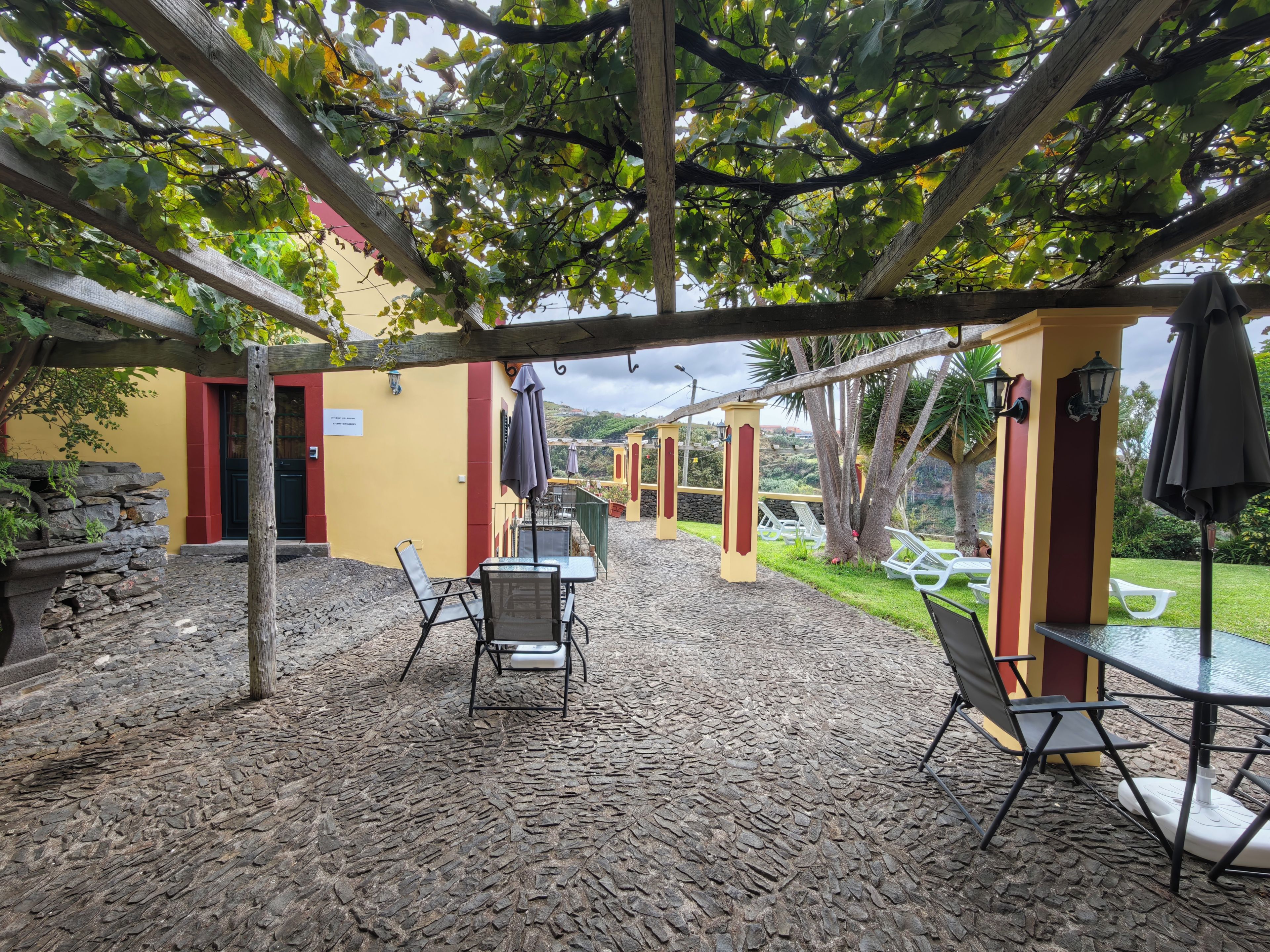 An outdoor patio with stone flooring, wooden pergola, and tables with chairs.