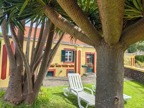 A yellow building with red trim, a white chair, and a palm tree in the foreground. - Herdade do Pedregal # 3 (Ponta do Pargo)