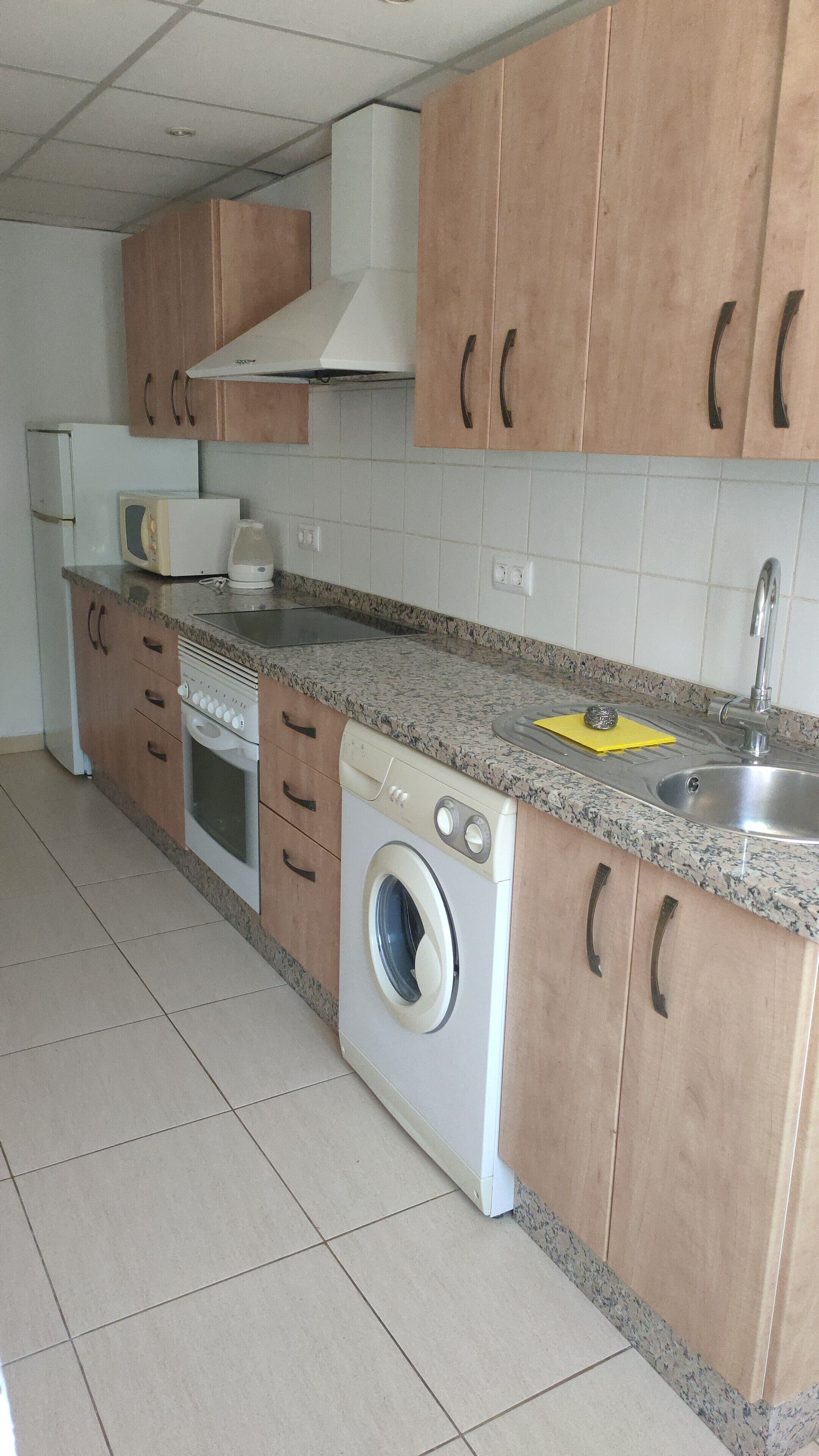Una cocina con armarios de madera, lavadora, microondas y un lavabo.