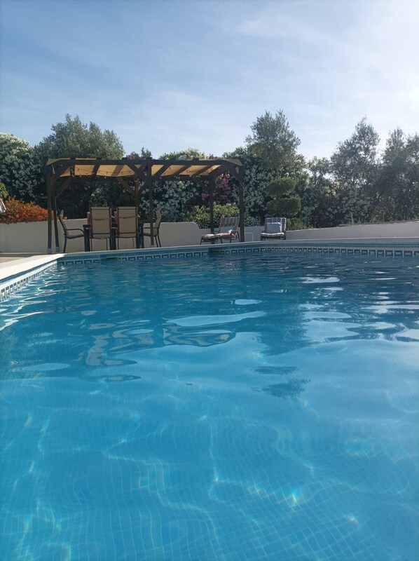 Ein klares Schwimmbecken mit einer Holz-Pergola und Liegestühlen.