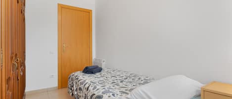 A bedroom with a bed, a wooden wardrobe, a white door, and a small bedside table.