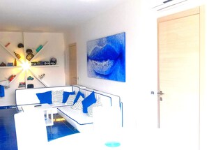 Un salon moderne avec un canapé blanc, des coussins bleus et un tableau abstrait bleu accroché au mur.