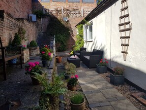 A courtyard with a brick wall, a wooden bench, wicker furniture, and potted plants. -   Hidden Cottage for Two in Cheadle Staffordshire, ideal for the  Peak District. (Cheadle)
