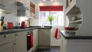 Una cocina compacta con horno empotrado, un tostador rojo y un ventanal con un adorno rojo.