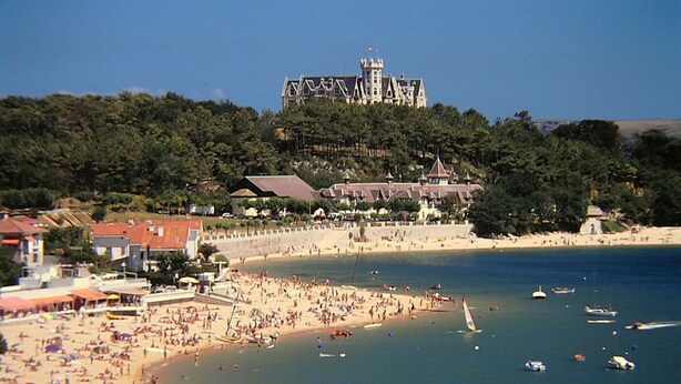 Ein Strand mit einem schlösserartigen Gebäude im Hintergrund.