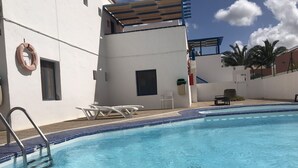 A swimming pool with clear blue water, surrounded by white walls and a few lounge chairs. - Delia Castillo Vacation Home  (Castillo Caleta de Fuste)