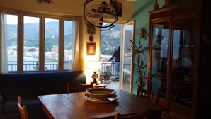 A dining area with a table, chairs, and a view of a balcony with a person outside. - Amazing panoramic terrace in Castel di Tusa - air conditioning & wi-fi (Tusa (me))