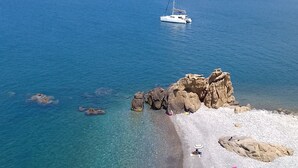 A beach with clear turquoise water, rocky formations, and a sailboat in the distance. - Amazing panoramic terrace in Castel di Tusa - air conditioning & wi-fi (Tusa (me))