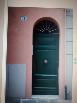 A green door with a number 36 sign above it, set in a building with a red wall and a small window to the left.