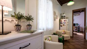 Una habitación bien iluminada con un tocador blanco, dos plantas en macetas, un sofá y una mesa.