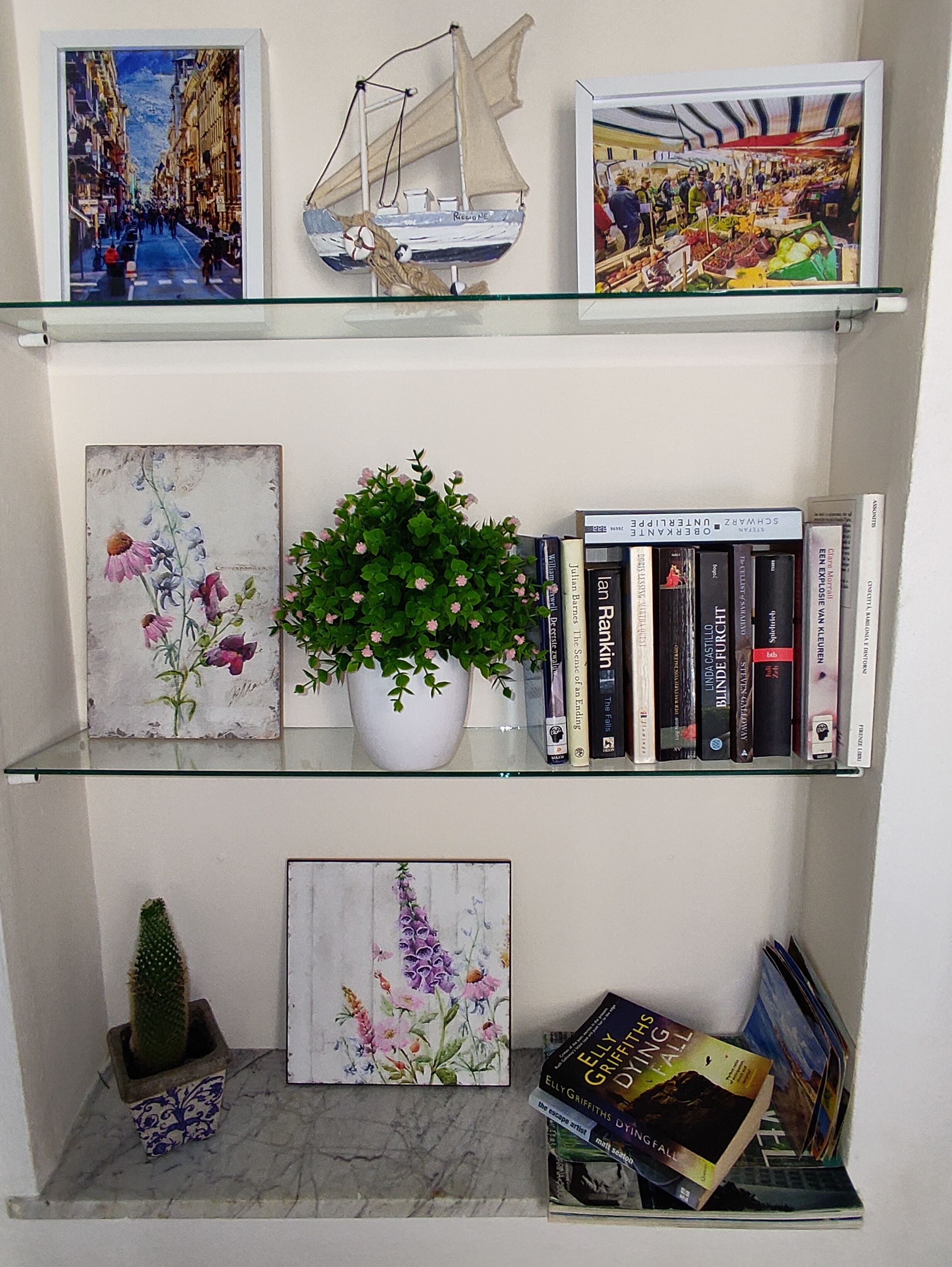 A shelf with a sailboat model, framed artwork, a potted plant, and books.
