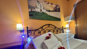 A neatly made bed with folded towels and a decorative pillow, a painting of a coastal scene on the wall, and two wall-mounted lamps. - One Bedroom Apartment   for 2/4 people (Gemini) (assisi)