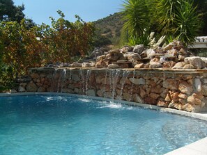 A swimming pool with a stone waterfall feature, surrounded by rocks and greenery. - September with climate of 30 C plus for the month so come and enjoy yourselves. (Iznajar,Cordoba)