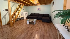 A spacious living room with a wooden staircase, a dark sofa, a glass coffee table, and a potted plant.