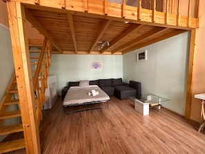 Une pièce de taille modeste comprenant un lit en mezzanine, un canapé et une petite table.