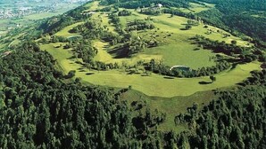 An aerial view of a golf course with multiple holes, surrounded by dense forest and distant cityscape. - Luxury cottage, big terrace, marvelous view (Brendola)