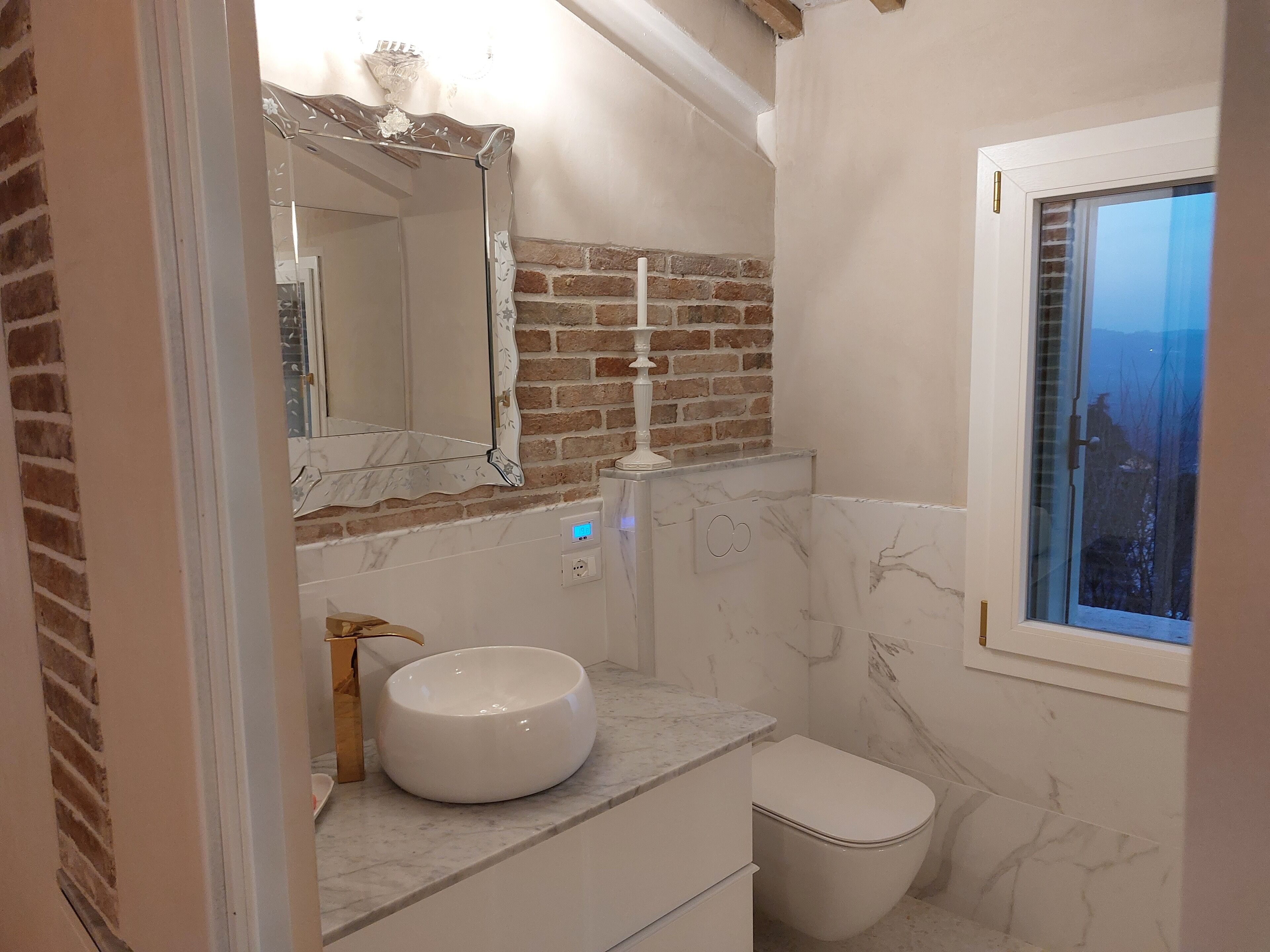 Een badkamer met een marmeren wastafel, een wit toilet, een spiegel met decoratieve lijst en een bakstenen muur.