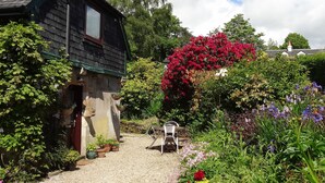 Een landelijke stenen woning met een grindpad en een tuin vol verschillende planten en bloemen.