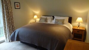 Een keurig opgemaakt bed met een donkere sprei, twee bedlampen en een klein houten nachtkastje met een lamp.