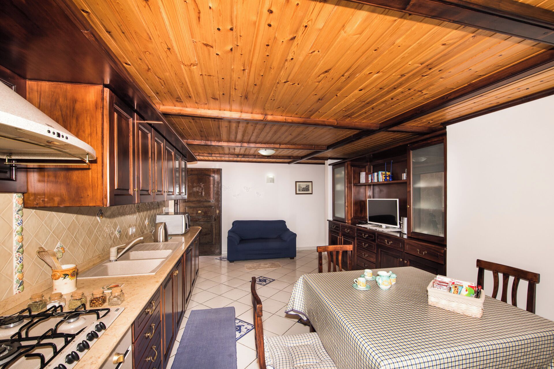 A compact kitchen with a gas stove, wooden cabinets, and a blue sofa in the living area.