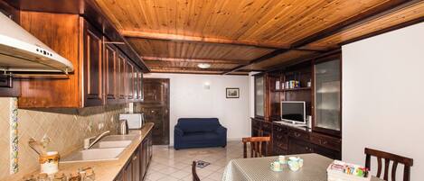 A compact kitchen with a gas stove, wooden cabinets, and a blue sofa in the living area.