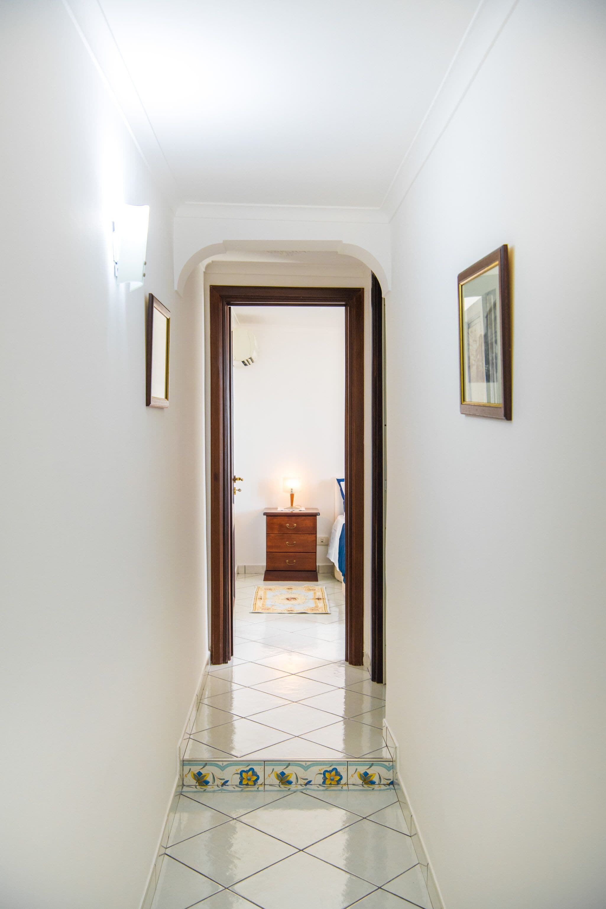 A hallway with a tiled floor, a wooden door, and a small table with a lamp.