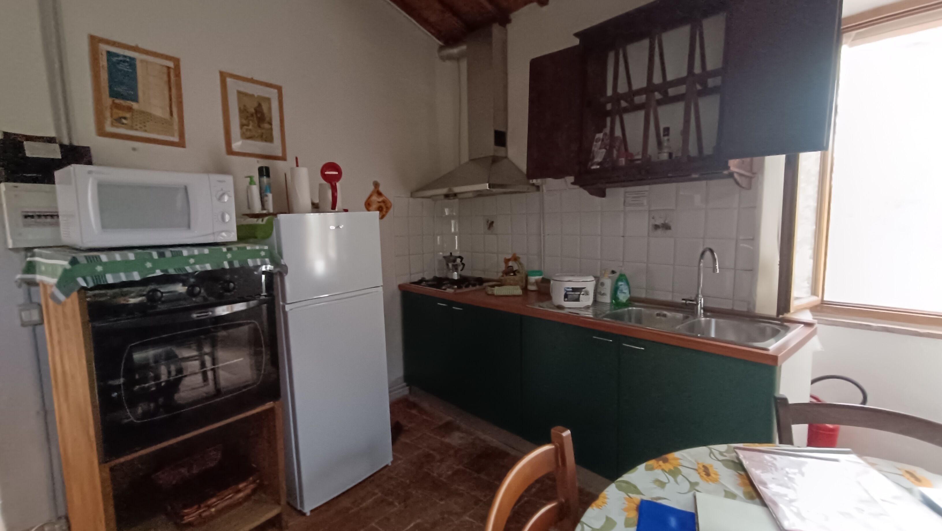 A compact kitchen with a stove, oven, microwave, and sink. There is a table with chairs and a window with curtains.