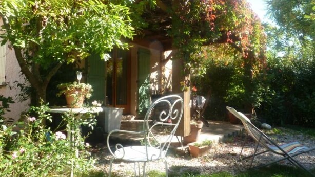 Un jardín con una silla de metal, una mesa y una pequeña estructura con una puerta.