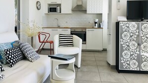 Ett modernt kök med vita skåp, en mikrovågsugn och en kaffebryggare. Det finns en matplats med en vit stol och ett litet bord.
