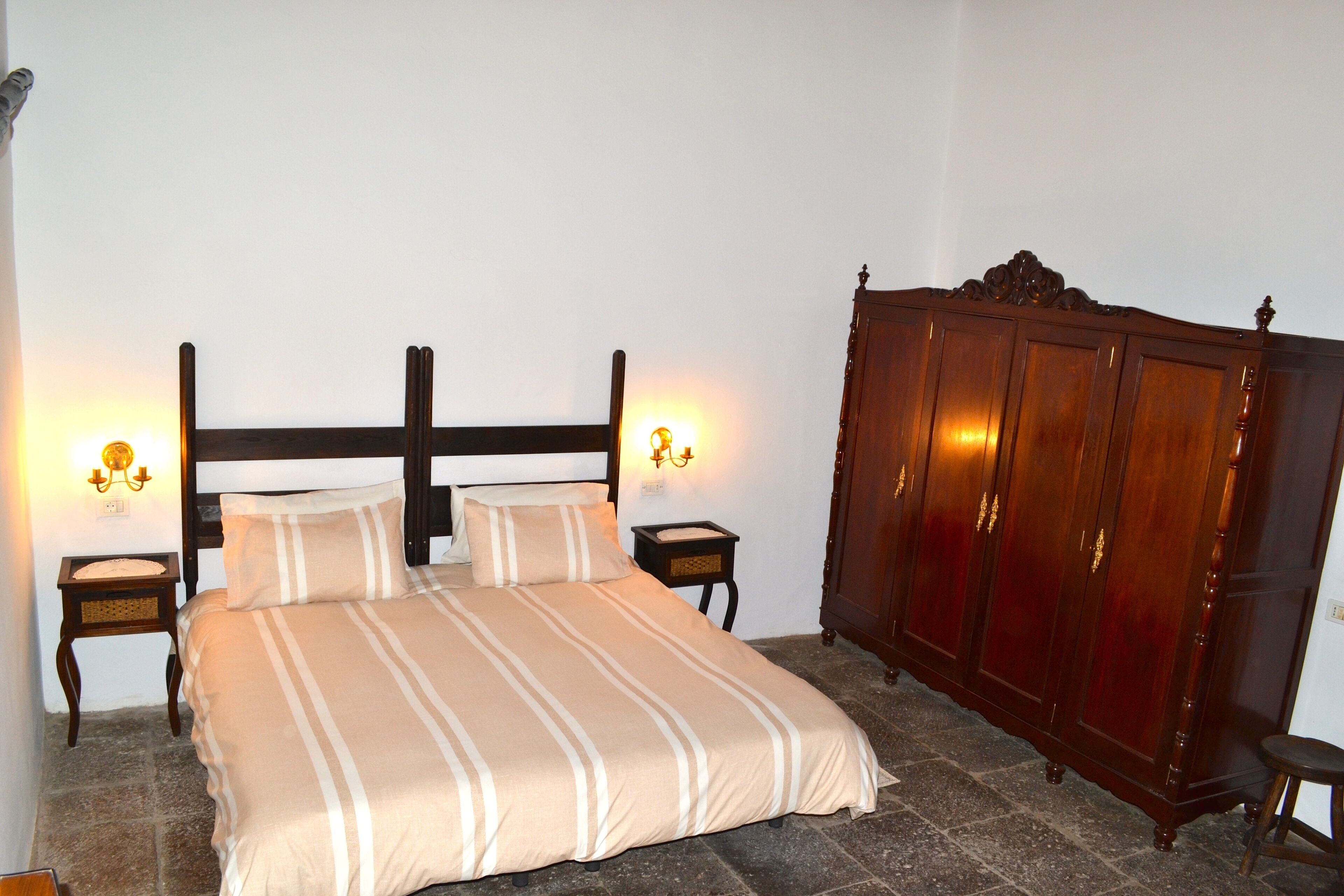 A bedroom with a bed, two bedside tables, a wooden wardrobe, and wall-mounted lights.