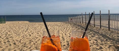 A beachside table with two glasses of orange beverage, a bowl of ice cream, and a smartphone on a white tray.