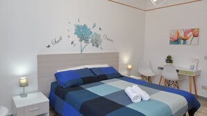 Una cama bien tendida con una colcha azul y negra a cuadros, una mesita de noche blanca con una lámpara, y una pared con un mural floral y la inscripción 'Sweet Dreams'.
