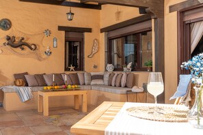 A cozy seating area with a wooden bench and a table, decorated with fruits and a glass of white wine.