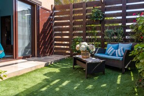 A patio with a wicker sofa, a small table, and a wooden fence.
