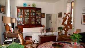 A living room with a white sofa, a wooden cabinet with books, a coffee table, and a decorative sculpture. - For My Friends B & B - Sun Room (Roma)